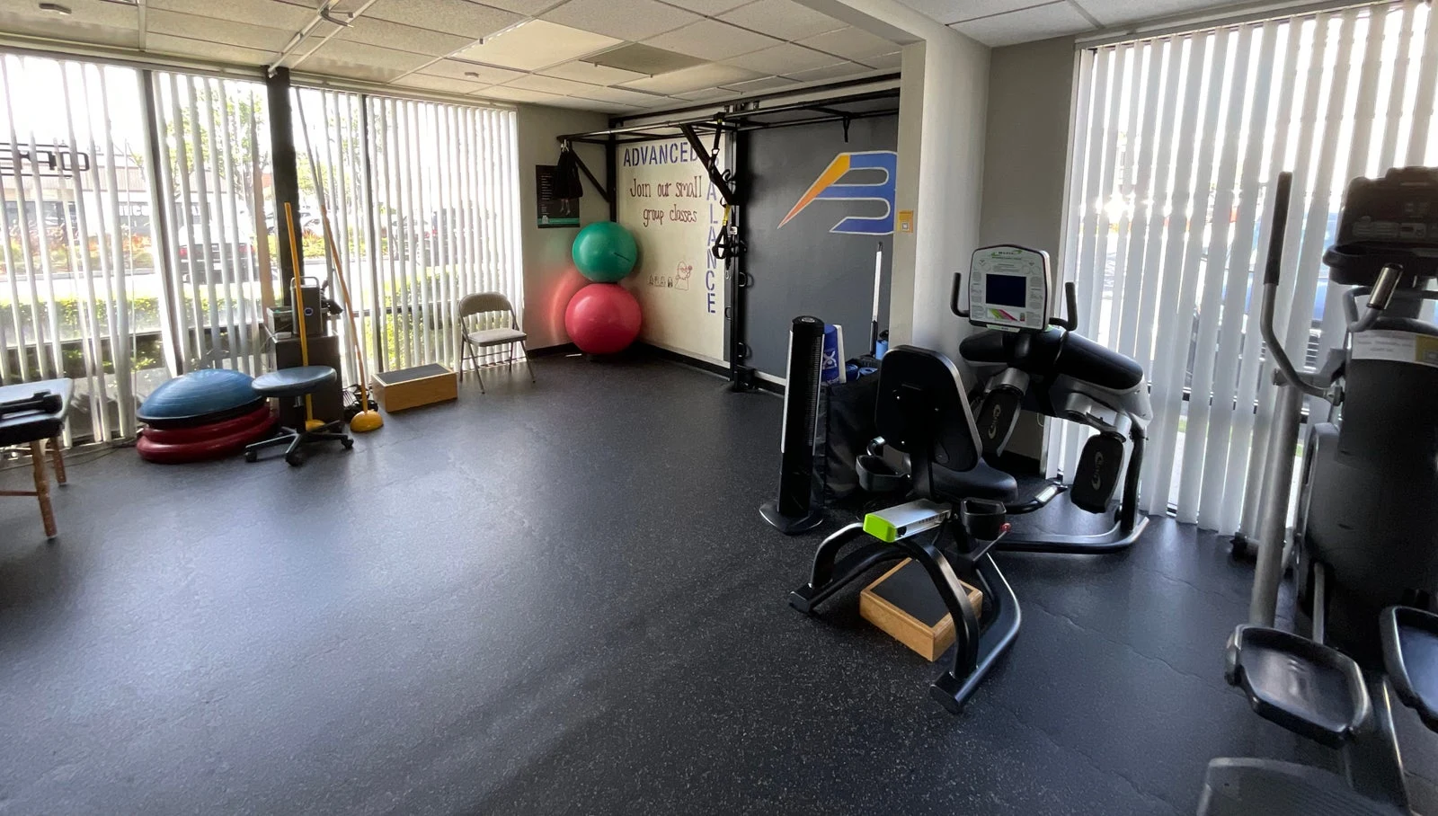 The exercise space at Advanced Balance with its blue-and-yellow wall logo and rehabilitation equipment